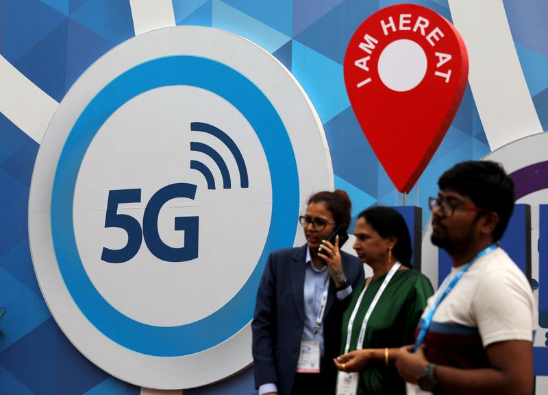 People stand in front of a board depicting 5G network at the India Mobile Congress 2018 in New Delhi