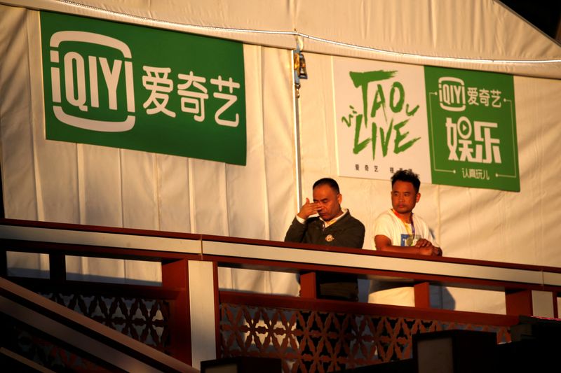 FILE PHOTO: Men stand near a booth with signs for iQIYI during the Beijing International Film Festival