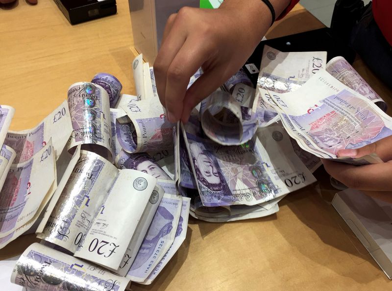 FILE PHOTO: A shop assistant counts piles of British Pound Sterling banknotes at an Apple store in London