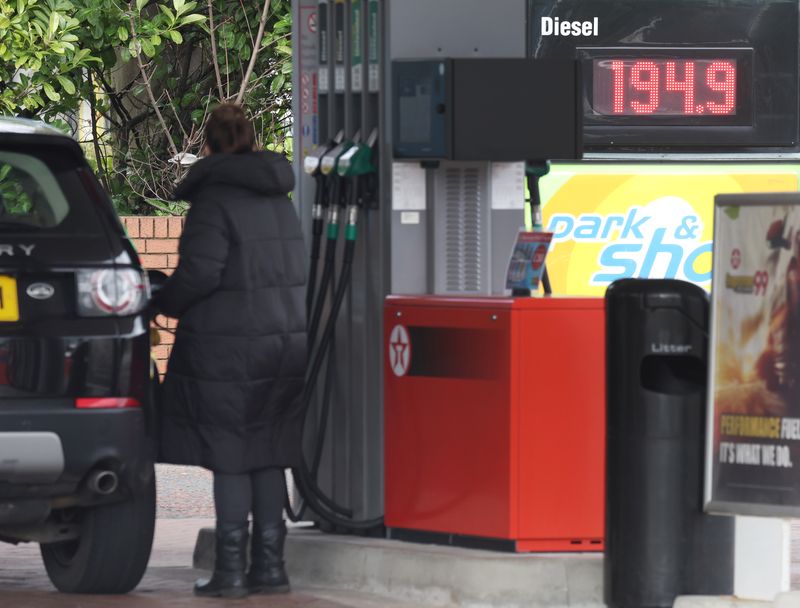 Woman fills up her car in front of a sign showing increased fuel prices at a filling station near Liverpool
