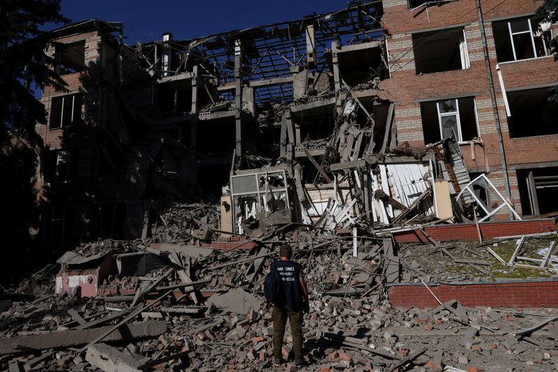 FILE PHOTO: A worker from the war crimes prosecutor's office takes in the damage from overnight shelling that landed on a building of Kharkiv's Housing and Communal College