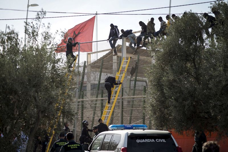 FILE PHOTO: African migrants sit on top of a border fence during an attempt to cross into Spanish territories, between Morocco and Spain's north African enclave of Melilla