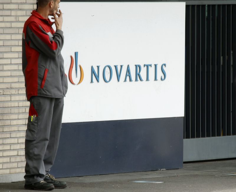 An employee smokes a cigarette beside the logo of Swiss drugmaker Novartis AG in front of a plant in Basel