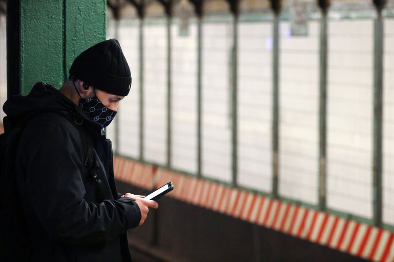 A person uses a smartphone on a subway platform in Manhattan, New York City