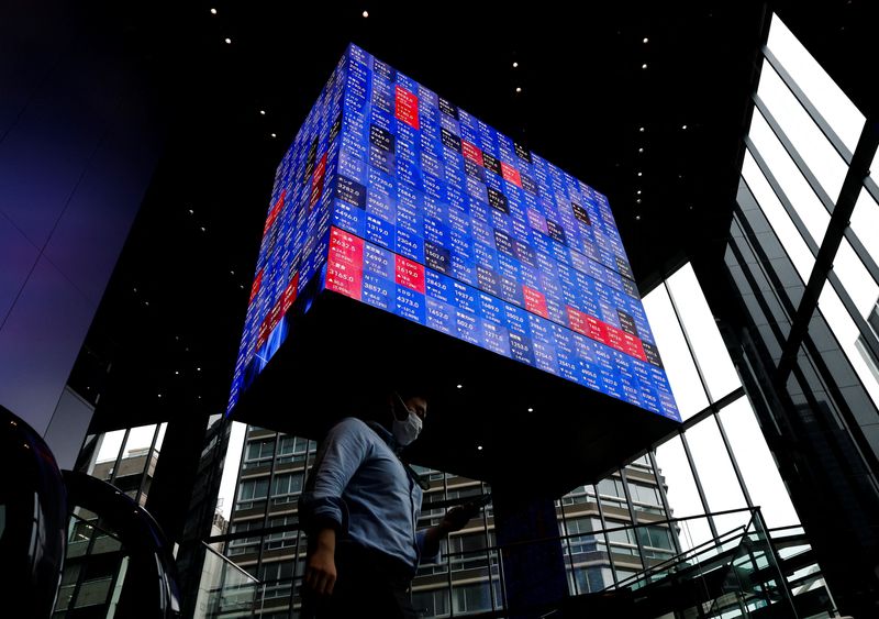 People pass by an electronic screen showing Japan's Nikkei share price index inside a conference hall  in Tokyo