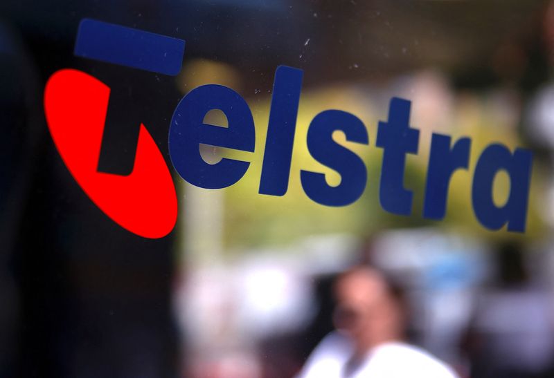 FILE PHOTO: A pedestrian walks past a Telstra logo adorning a phone booth in the central business district of Sydney