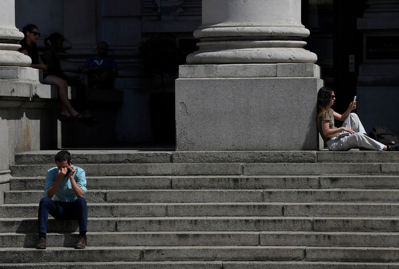 FILE PHOTO: People sit outside near the Bank of England during the hot weather in the City of London financial district, London