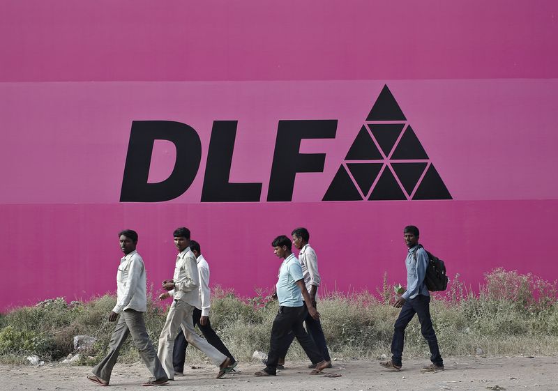 Workers walk past a billboard of DLF Ltd. at Gurgaon on the outskirts of New Delhi