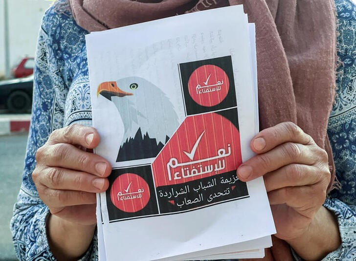 FILE PHOTO: A volunteer displays a campaign flyer for an upcoming referendum on a new constitution, in Kairouan