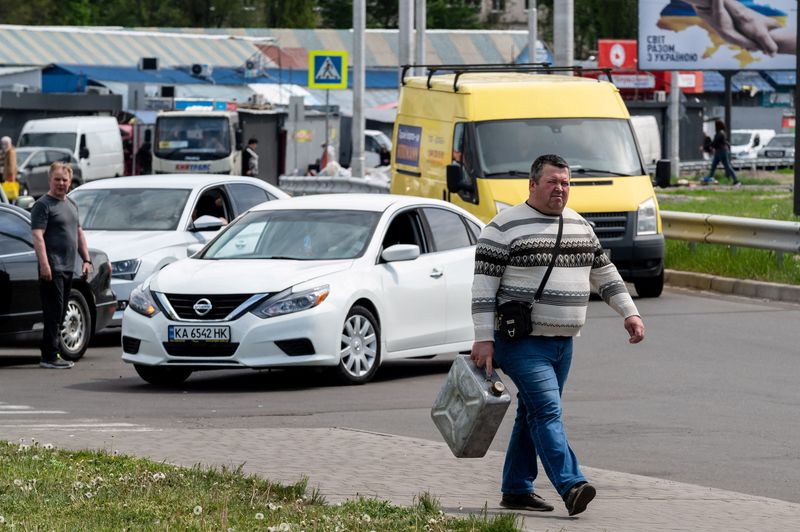 FILE PHOTO: A man with a jerry can walks next to a petrol station as drivers stay in line trying to buy fuel in Kyiv
