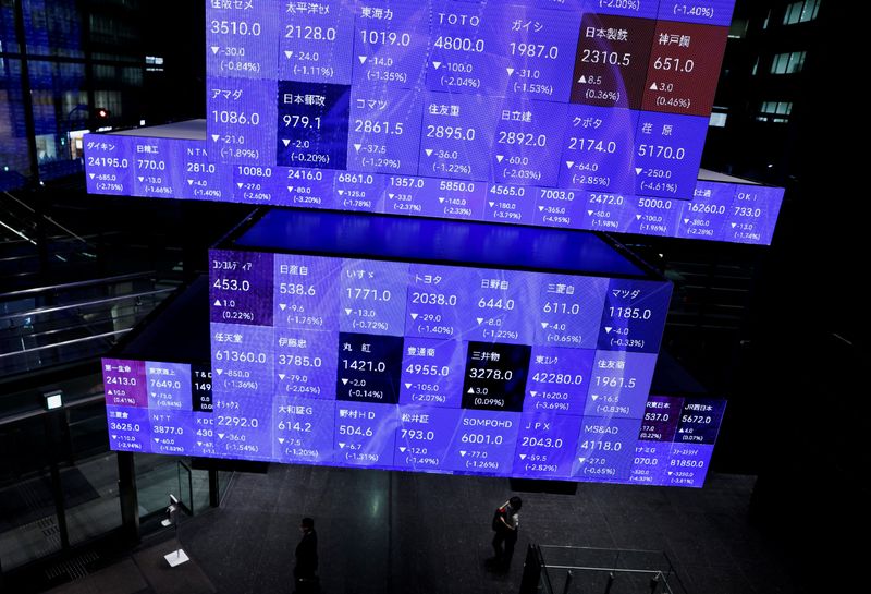 FILE PHOTO: Visitors walk past Japan's Nikkei stock prices quotation board inside a conference hall in Tokyo