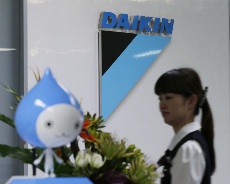 A staff walks past a logo of Daikin Industries Ltd and the company mascot 