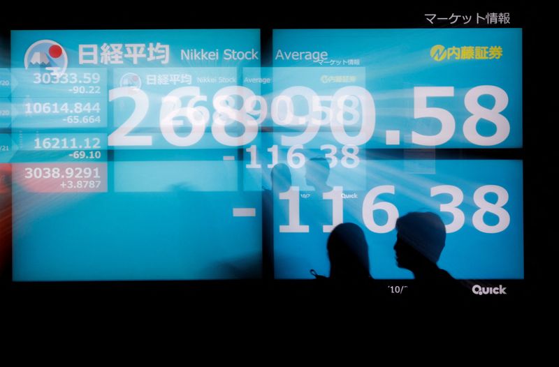 Silhouettes of passerby are seen as they walk in front of an electric monitor displaying Japan's Nikkei share average in Tokyo