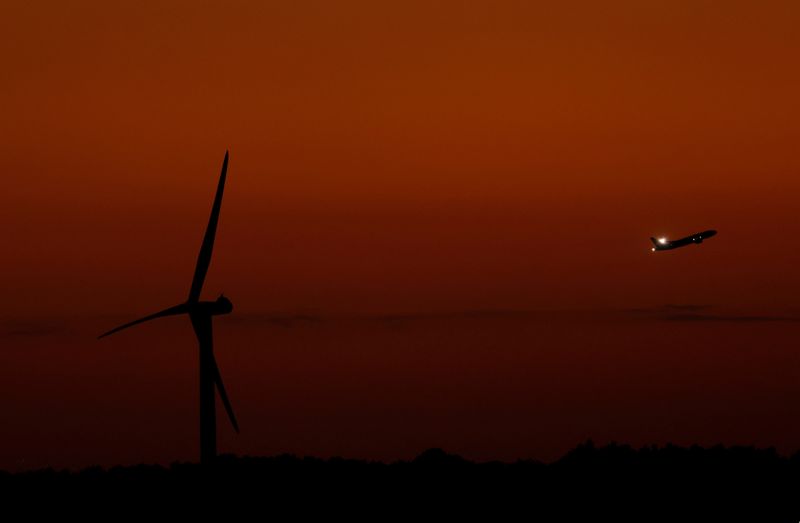 FILE PHOTO: A wind turbine is seen as a plane flies during sunset in Tokyo