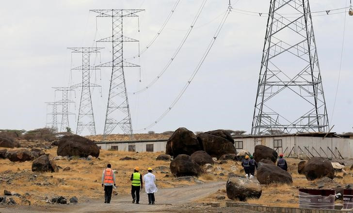 Workers walk near power lines connecting pylons of high-tension electricity from the power substation at the Lake Turkana Wind Power project in Loiyangalani district, Marsabit County
