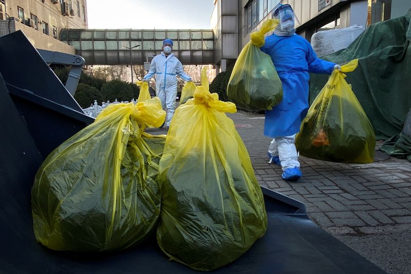Workers in protective suits remove bags of medical waste outside a building where residents isolate at home as coronavirus disease (COVID-19) outbreaks continue in Beijing